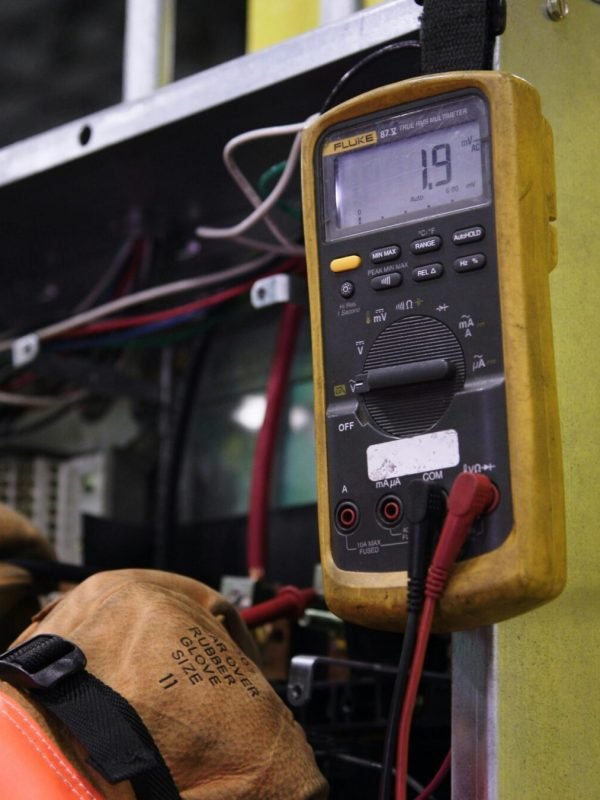 Electrician using a multimeter to fix industrial control panel wiring.