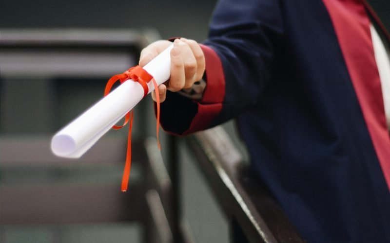 A close-up image of a graduate holding a diploma tied with a red ribbon, symbolizing achievement and success.